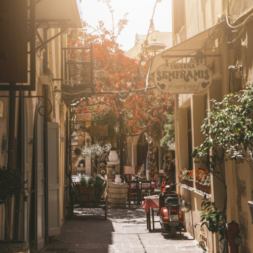 A small thin walkway between building covered in hanging baskets in bloom