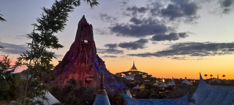 Evening view of the Volcano Bay water park with glowing lights, slides, and volcano silhouette from Cabana Bay Resort