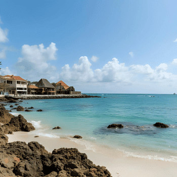 Sandy beach with rocky shoreline, turquoise ocean, and villas by the water under a bright sky
