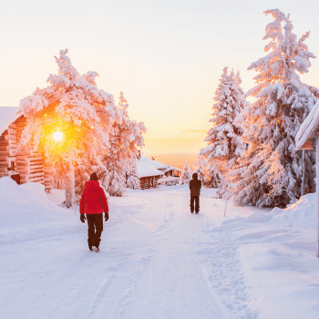 People walking among snowy cabins and trees at sunset in Rovaniemi, Lapland, Finland