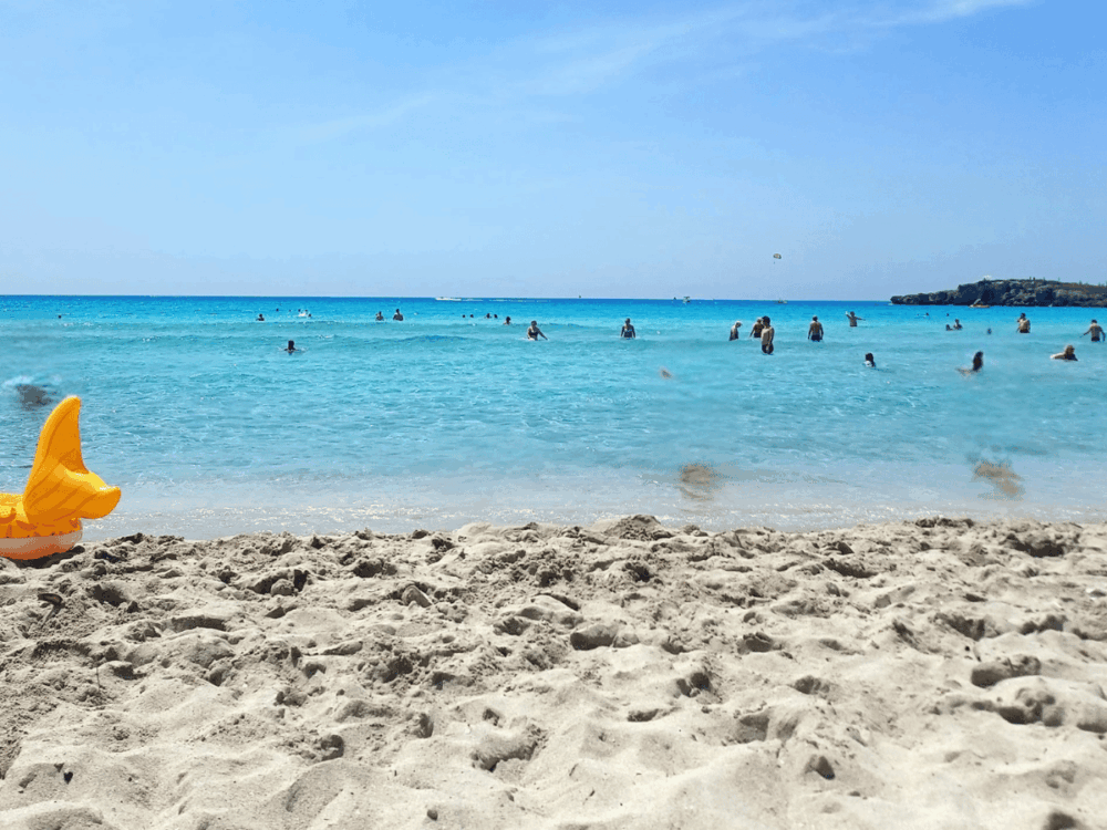 Sandy beach and turquoise sea with people swimming at Nissi Beach