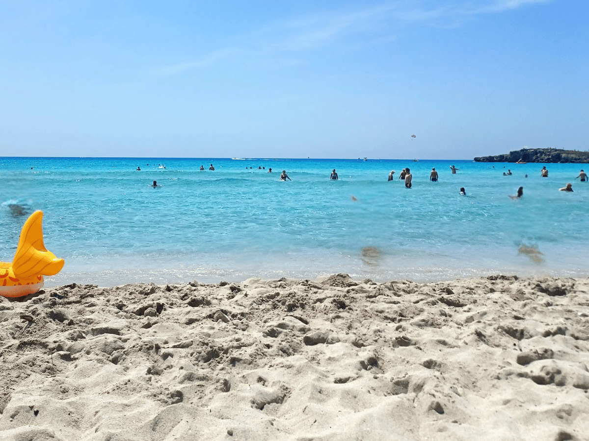 Sandy beach and turquoise sea with people swimming at Nissi Beach
