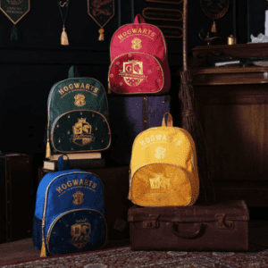 Four Harry Potter alumni backpacks in house colours – Slytherin green, Gryffindor red, Ravenclaw blue, and Hufflepuff yellow – displayed in a wizard-themed room.