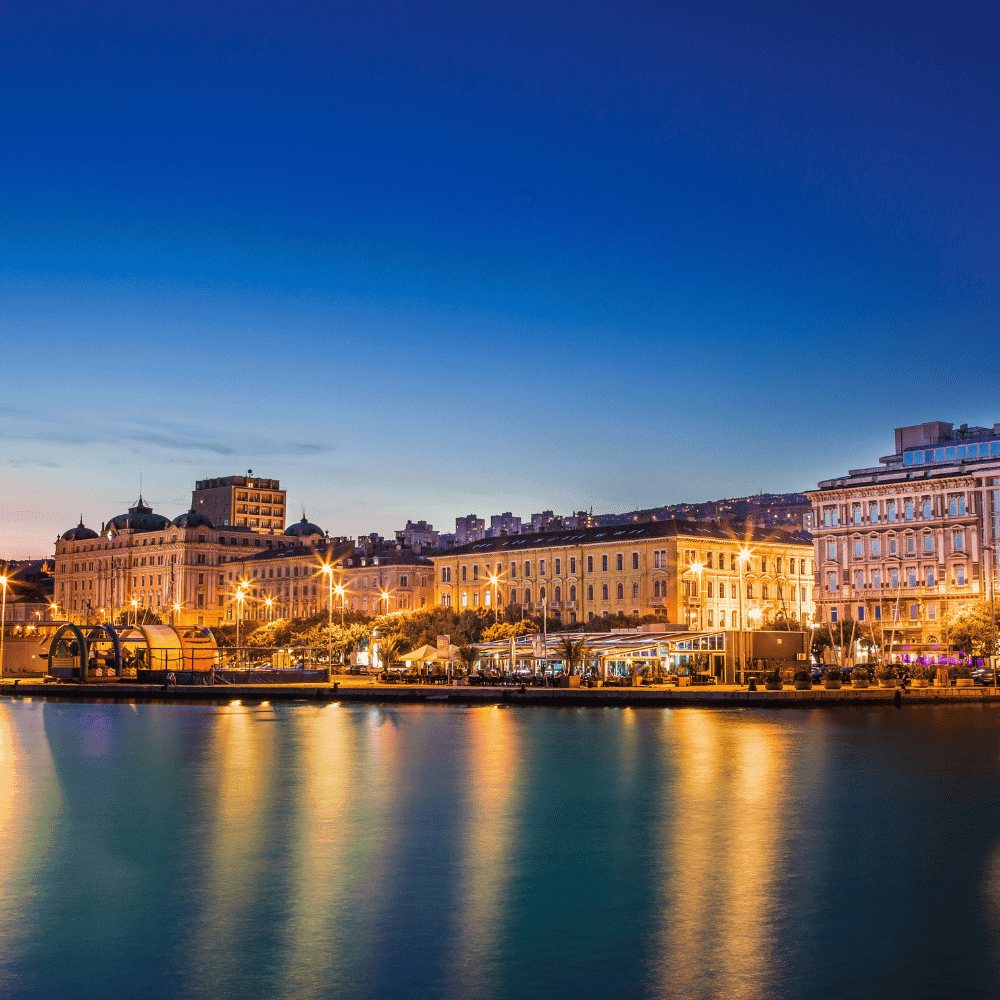 Evening view of the Rijeka waterfront with glowing lights reflecting across the water.