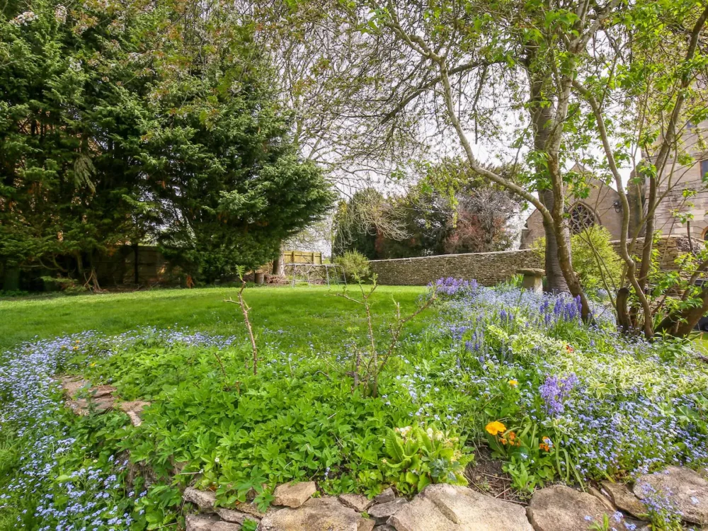 Compare Flights and Travel Essentials 81 Peaceful garden at Japonica Cottage in Bourton-on-the-Water with green lawn, trees and spring flowers