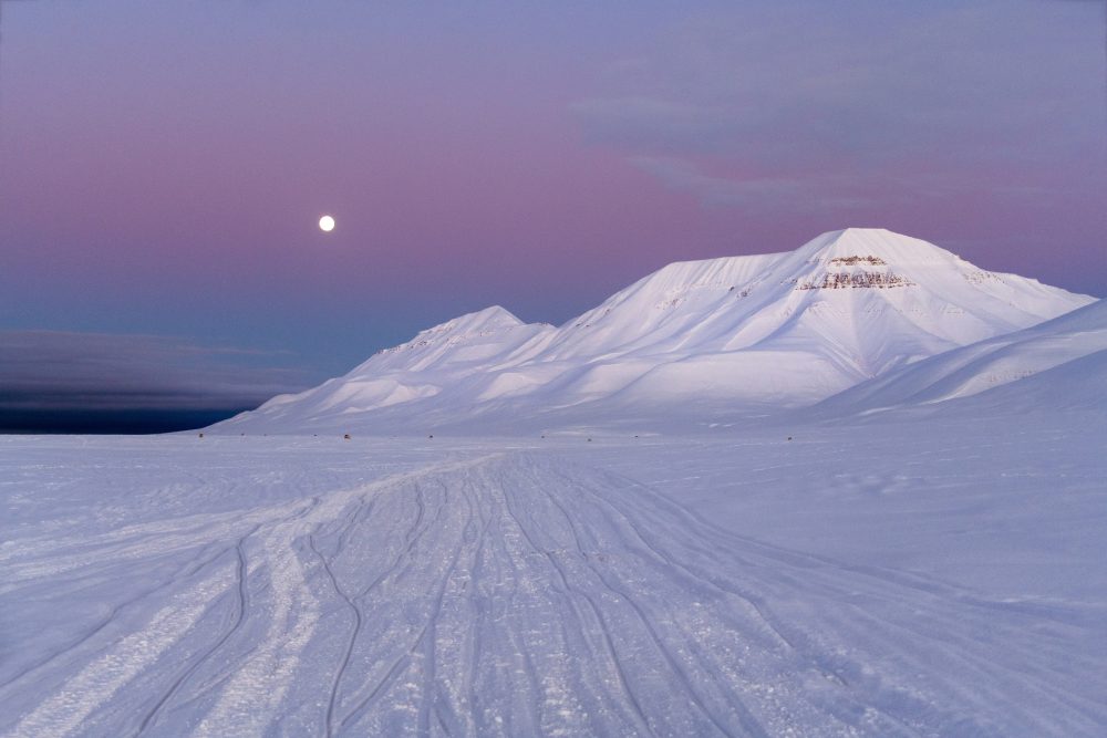 Snow-covered Arctic mountains in Svalbard beneath a soft polar sky and rising moon