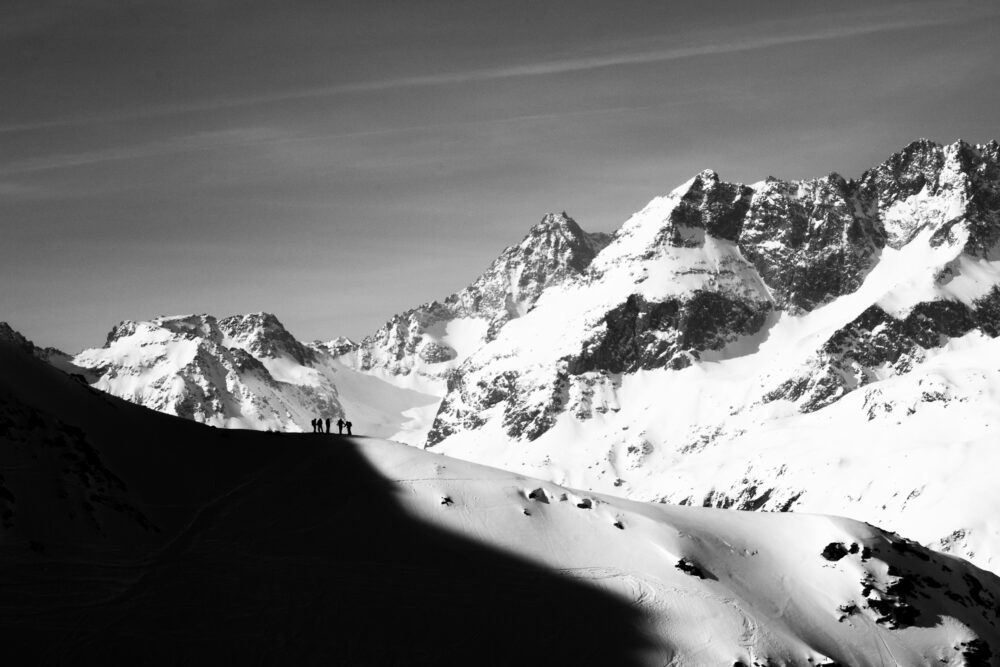 Compare Flights and Travel Essentials 74 Silhouetted hikers standing on a snowy mountain ridge with dramatic alpine peaks behind