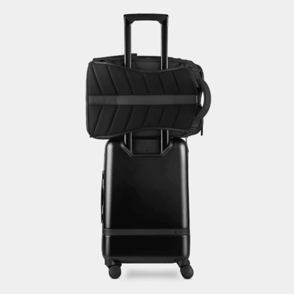 Backpack 1 Black Gomatic backpack attached to the handle of a rolling suitcase using the luggage pass-through strap during travel.