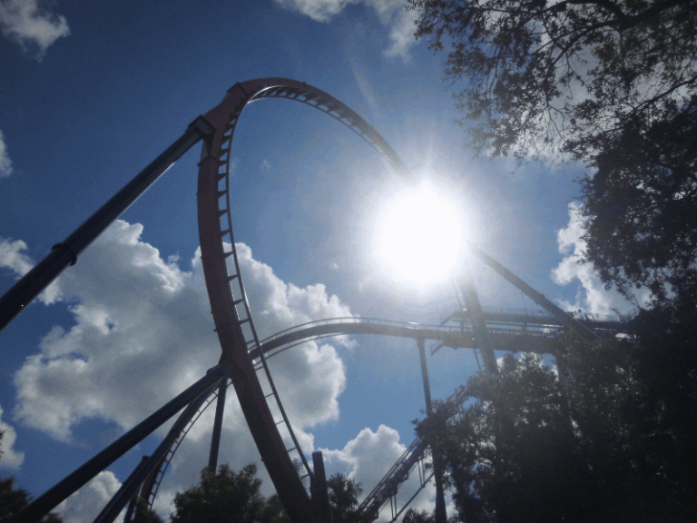 Roller coaster track silhouetted against bright sunshine and blue sky