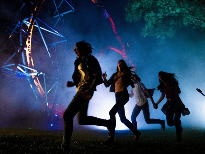 People running through a fog-filled scare zone at a theme park at night