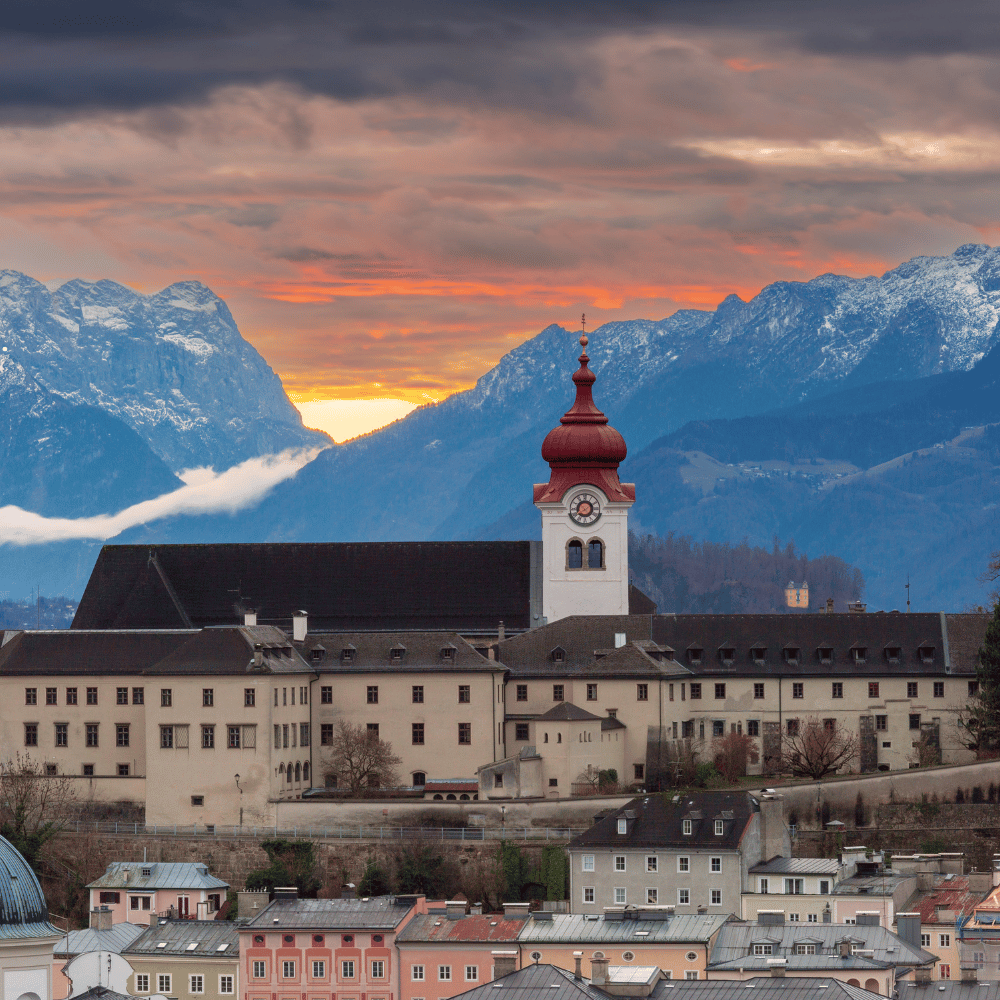 Salzburg rooftops and church tower with mountains at sunset