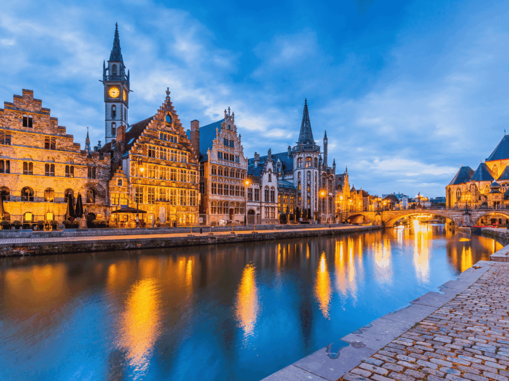 Historic canal and illuminated medieval buildings in Ghent, Belgium at dusk.