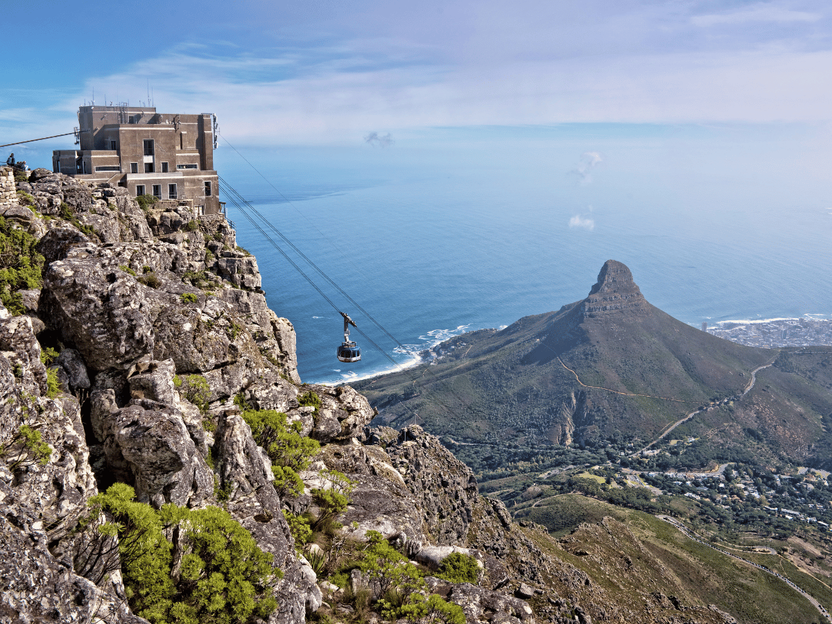 Cable car crossing Table Mountain with Lion's Head and Cape Town coastline below