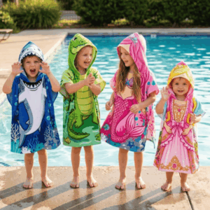 Four children wearing blue shark, green crocodile, pink mermaid and pink princess hooded poncho towels beside a swimming pool.