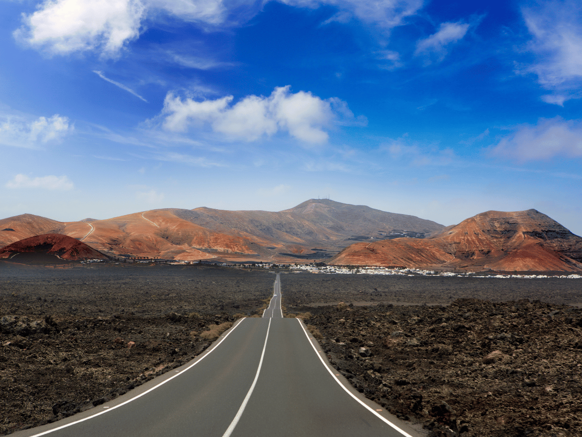 Road running through black volcanic landscape and reddish mountains in Lanzarote