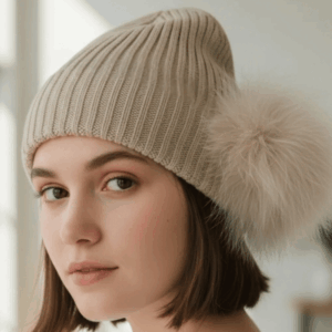 Person wearing a cream ribbed beanie with a large fluffy cream pom pom at the side.