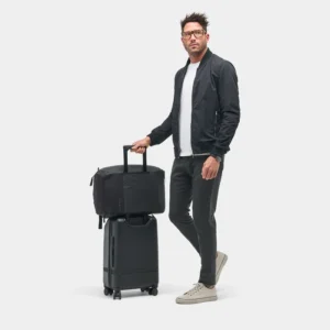 Person holding a black bag positioned on top of a wheeled suitcase