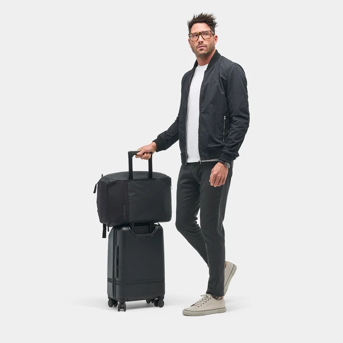 Person holding a black bag positioned on top of a wheeled suitcase