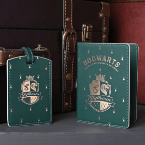 Green Slytherin passport holder and matching luggage tag with gold Hogwarts and Slytherin crest designs, displayed in front of vintage-style luggage.