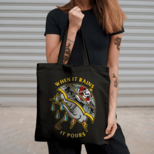 Black tote bag with long handles and colourful When It Rains It Pours umbrella artwork, carried over the shoulder by a person wearing black.