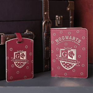 Red Gryffindor passport holder and matching luggage tag with gold crests and stars, displayed beside a dark brown travel trunk.
