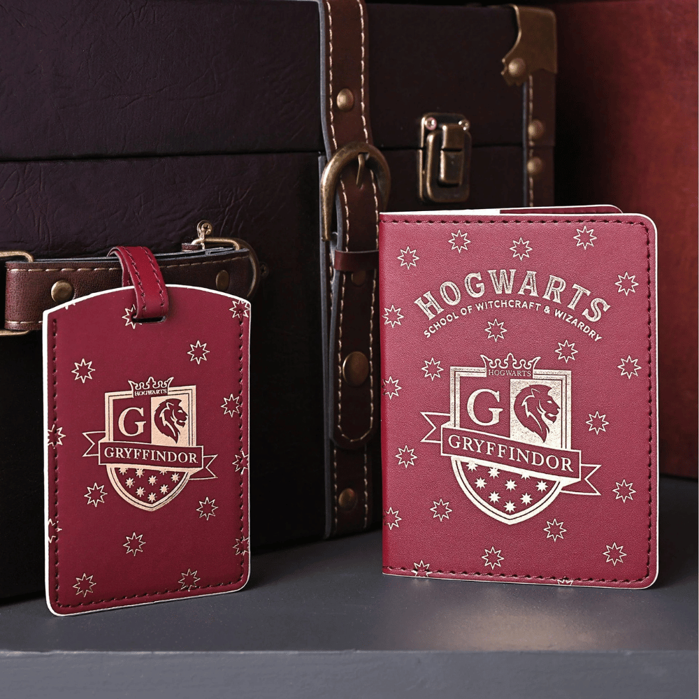 Red Gryffindor passport holder and matching luggage tag with gold crests and stars, displayed beside a dark brown travel trunk.
