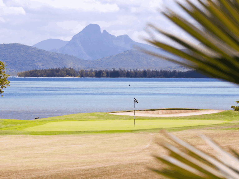 Golf green and sand bunker overlooking blue water and mountains in Mauritius.